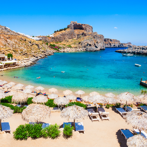 Sandy beach with straw umbrellas and lounge chairs beside a turquoise cove and rocky cliffs