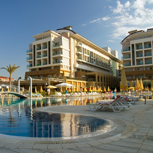 Luxury resort with pool, sun loungers, and umbrellas beside a multi-story hotel under a clear blue sky