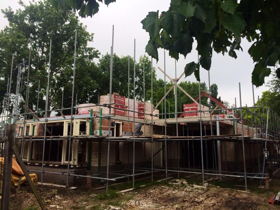 Een bouwplaats met een gedeeltelijk gebouwde bakstenen constructie, omgeven door een complex metalen steigersysteem.