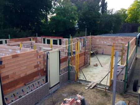 De muren van een bakstenen huis in aanbouw zijn gedeeltelijk gebouwd, met een deuropening en ondersteunende steigers.