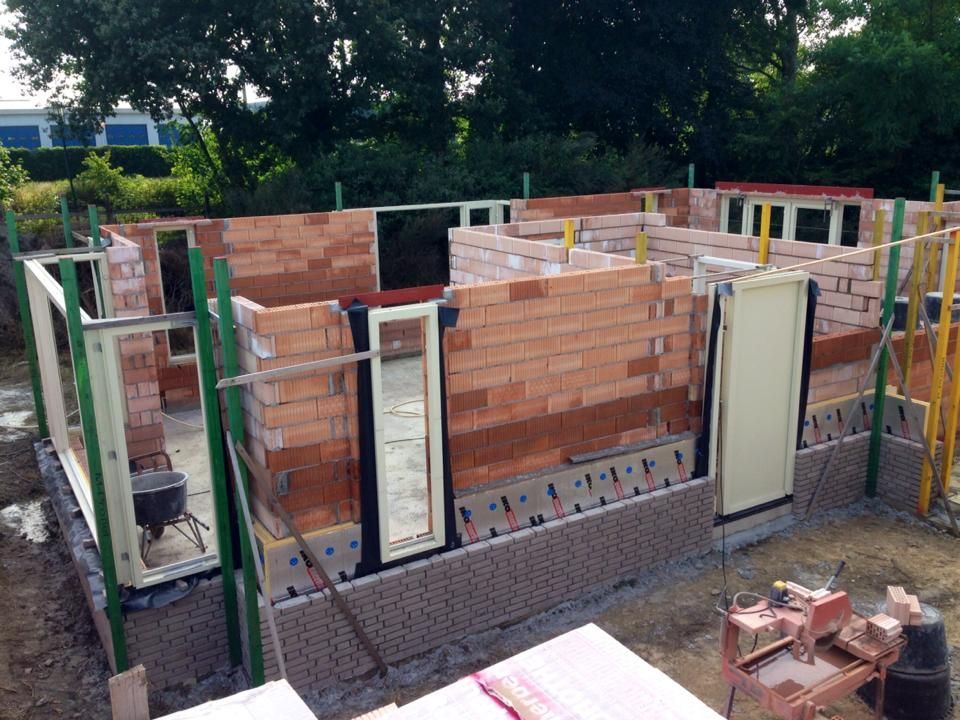 Een bouwplaats met half afgebouwde bakstenen buitenmuren, inclusief geplaatste raam- en deurkozijnen.