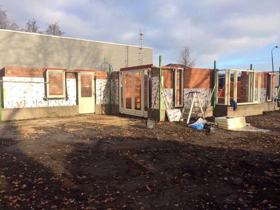 Een bouwplaats met een laag bakstenen gebouw dat wordt gerenoveerd, waarbij de raam- en deurkozijnen al zijn geplaatst.