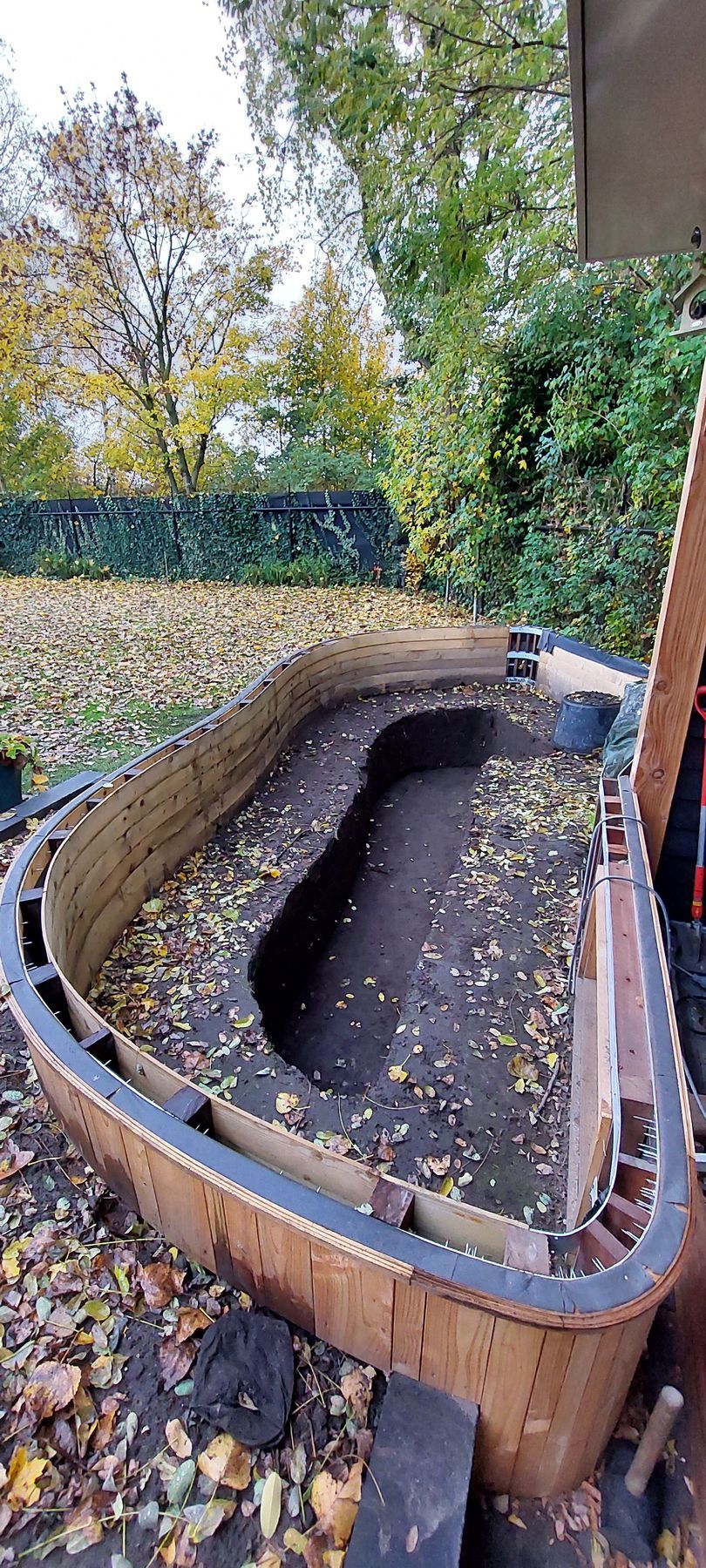 Een halvemaanvormige, verhoogde tuinbedconstructie gemaakt van bruine, geperforeerde plastic panelen, gevuld met donkere aarde en bladeren.