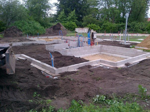 Een fundering van betonblokken voor een gebouw in aanbouw, omgeven door aarde en groene bomen.