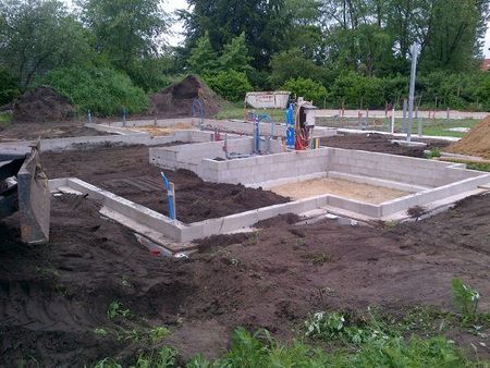 Fundamentmuren van betonblokken voor een nieuwbouwproject, omgeven door hopen donkere grond.