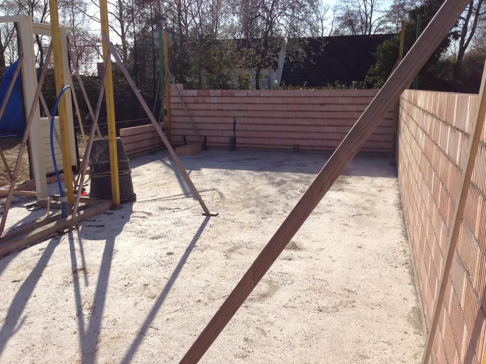 Bouwplaats met een betonnen fundering, omgeven door onafgewerkte bakstenen muren en metalen steunbalken.