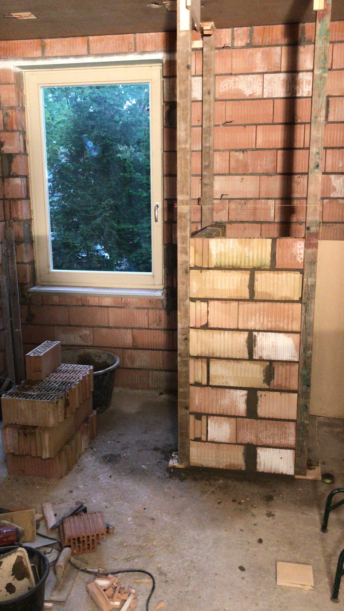 Een interieur van een bouwplaats met een pas gebouwde bakstenen pilaar naast een raam in een rode bakstenen muur.
