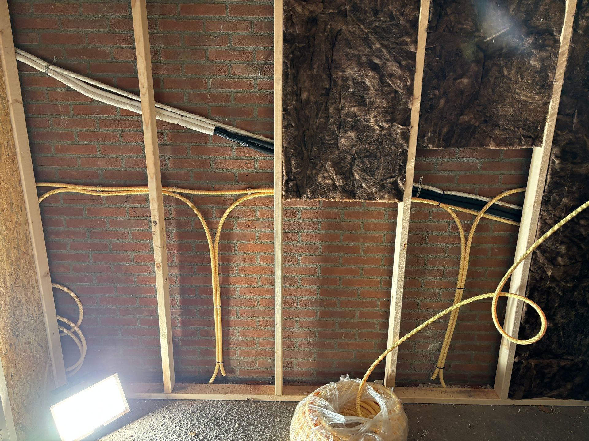 Gele elektriciteitskabels lopen langs een bakstenen muur met houten staanders, waarvan sommige gedeelten isolatie bevatten.