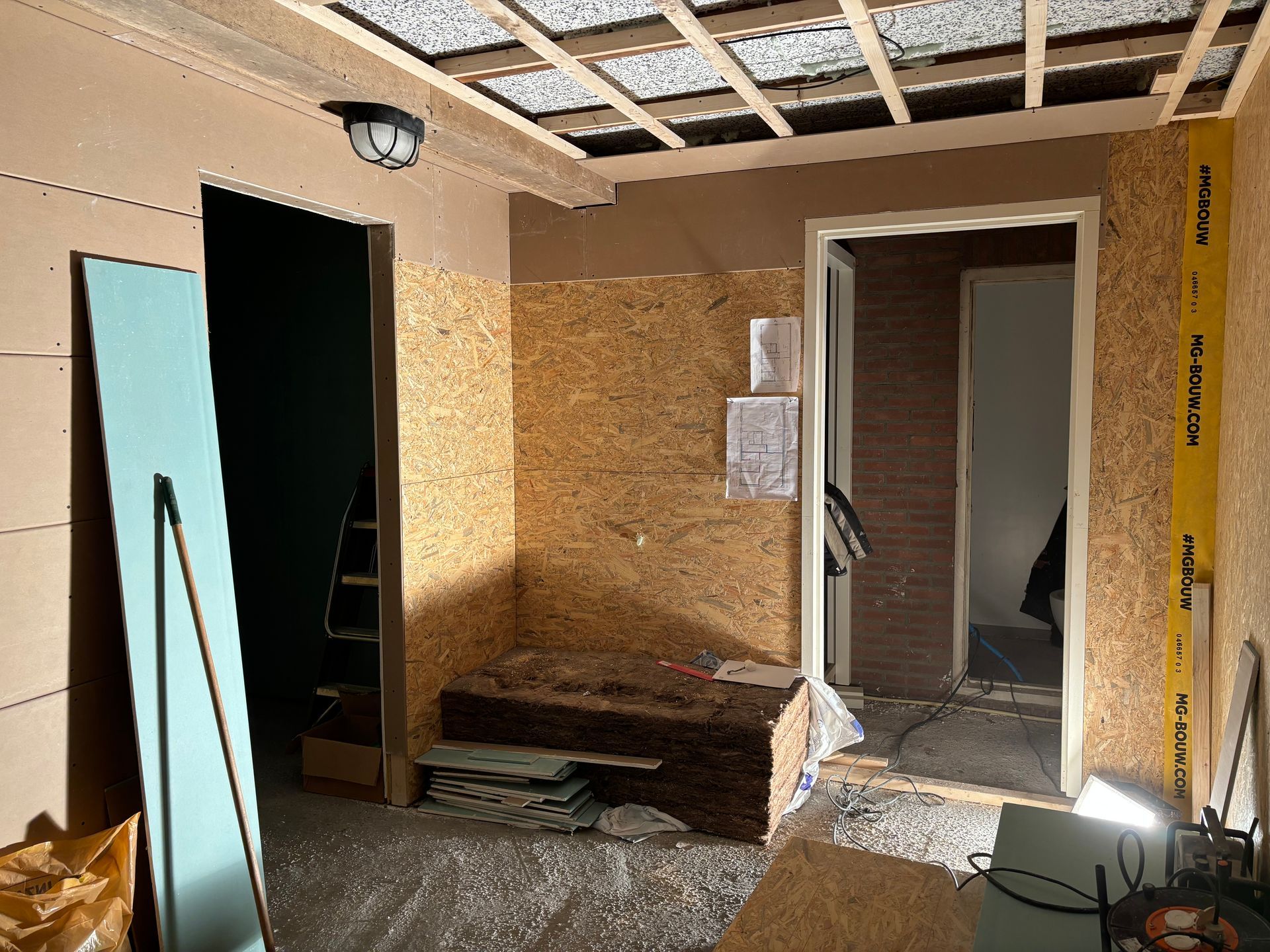 Een binnenruimte in aanbouw met OSB-beklede wanden, zichtbare plafondbalken en open deuropeningen.