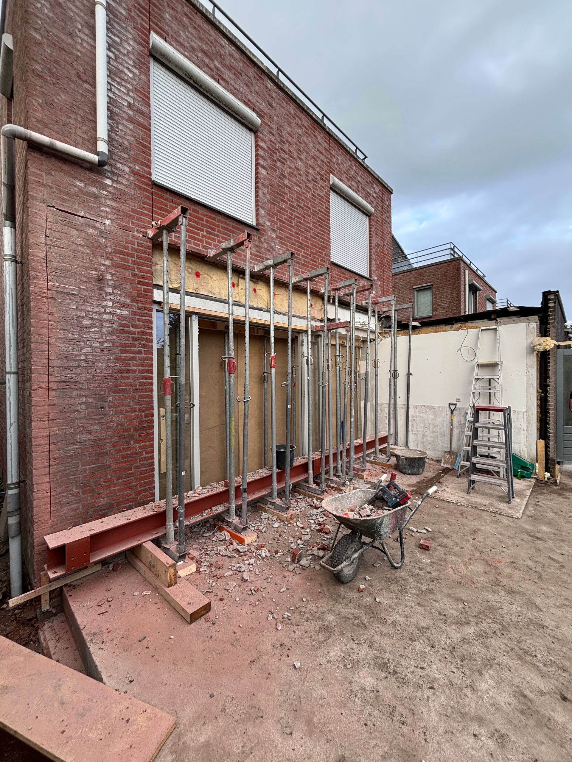 De buitenkant van een bakstenen gebouw in aanbouw, met een horizontale stalen balk die wordt ondersteund door meerdere metalen vijzels.