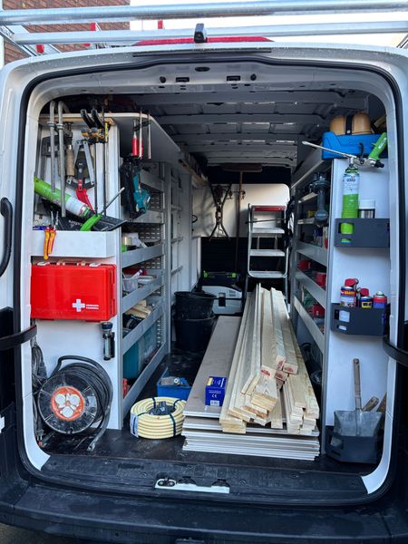 Het interieur van een witte bestelbus met georganiseerde schappen gevuld met gereedschap, apparatuur, een EHBO-doos en bouwmaterialen.