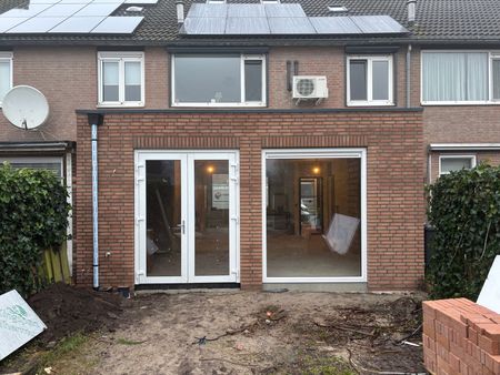 Een bakstenen huis met een recent aangebouwde uitbouw aan de achterzijde, voorzien van dubbele glazen deuren en een groot raam.