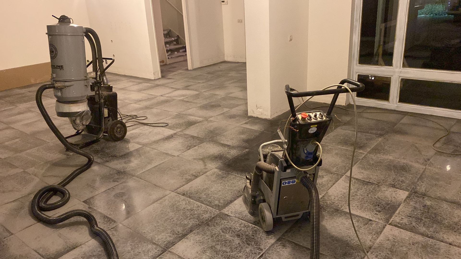 Twee industriële vloerschuurmachines en een stofzuigsysteem staan ​​tijdens renovatiewerkzaamheden op een betegelde binnenvloer.