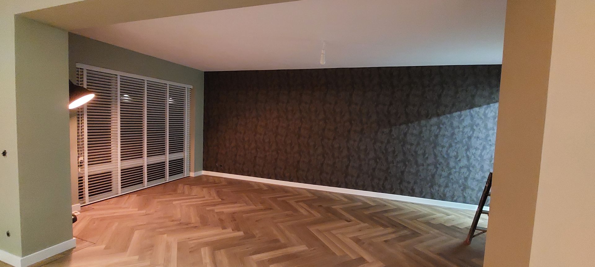 De ruime kamer is voorzien van lichte houten vloeren in visgraatpatroon, een donkere accentmuur met patroon en een decoratief kamerscherm.