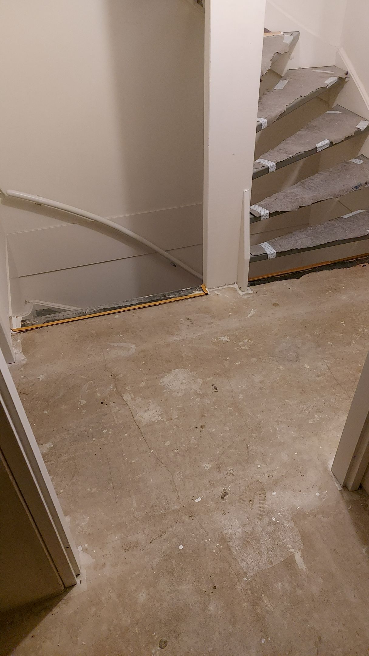Een uitzicht vanuit een gang op een onafgewerkte trap met kale houten treden en witte plinten.