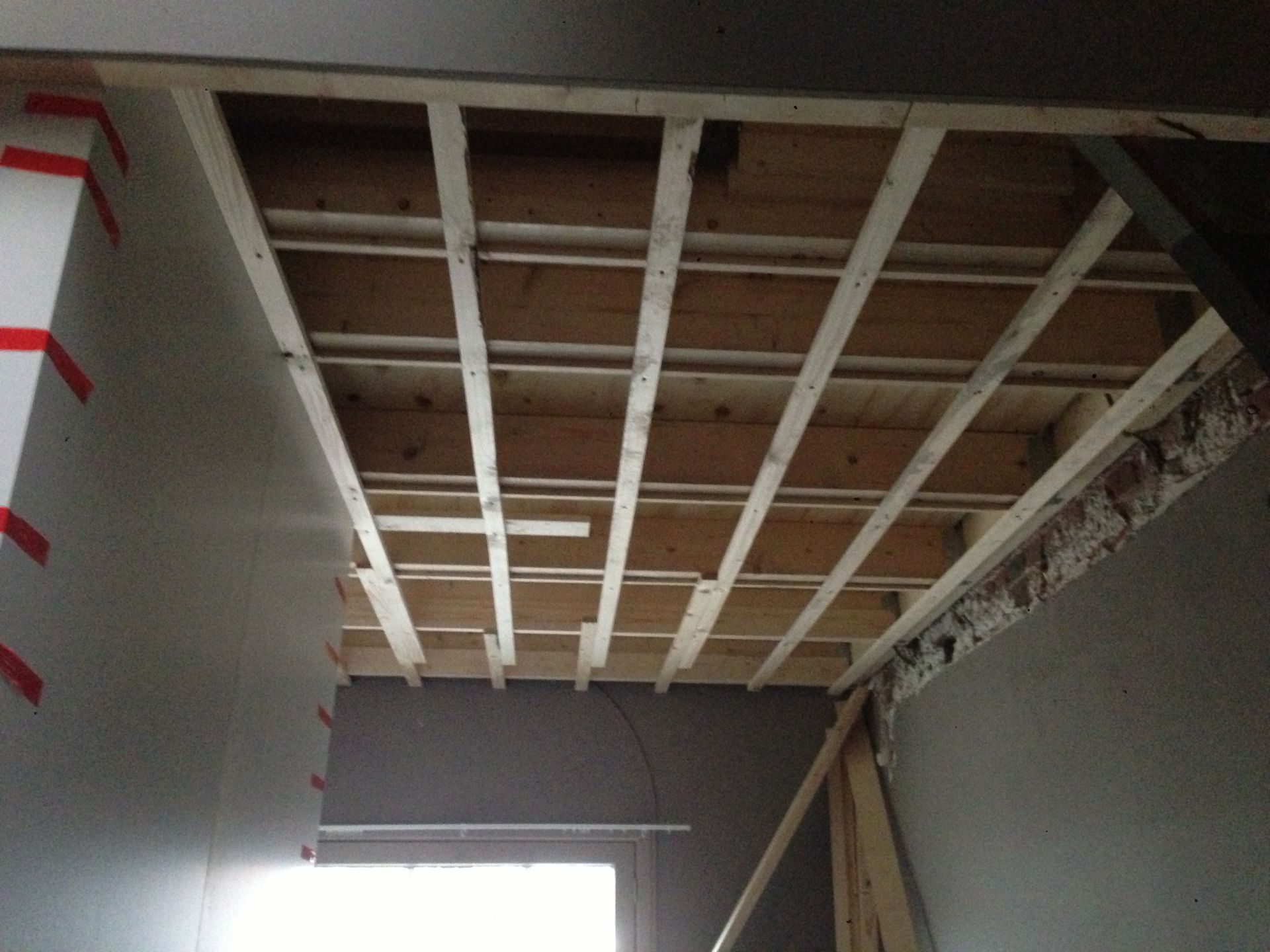 Een plafond in aanbouw, met houten balken die kruislings verstevigd zijn met witte latten.