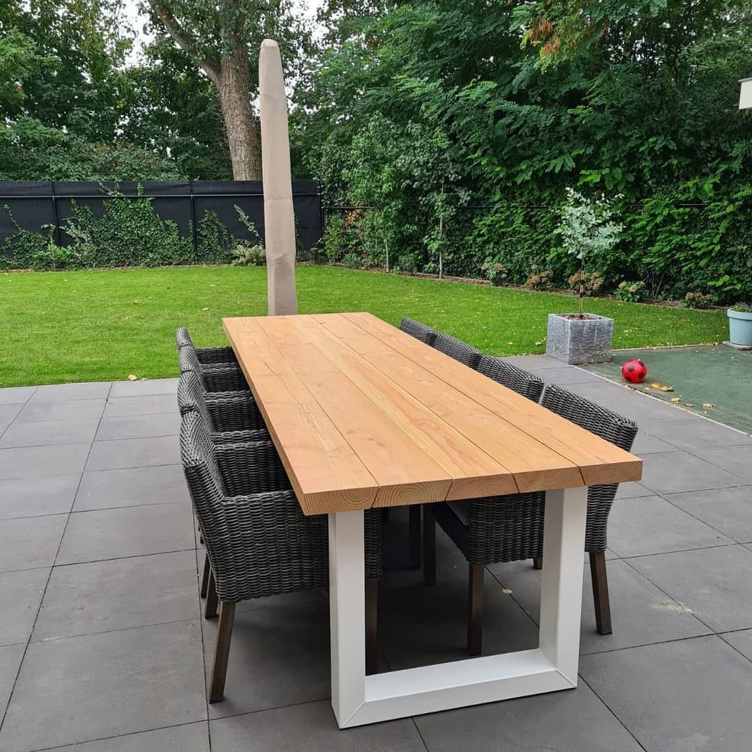 Een rechthoekige houten eettafel met een wit metalen frame, omringd door rieten stoelen op een grijs terras.