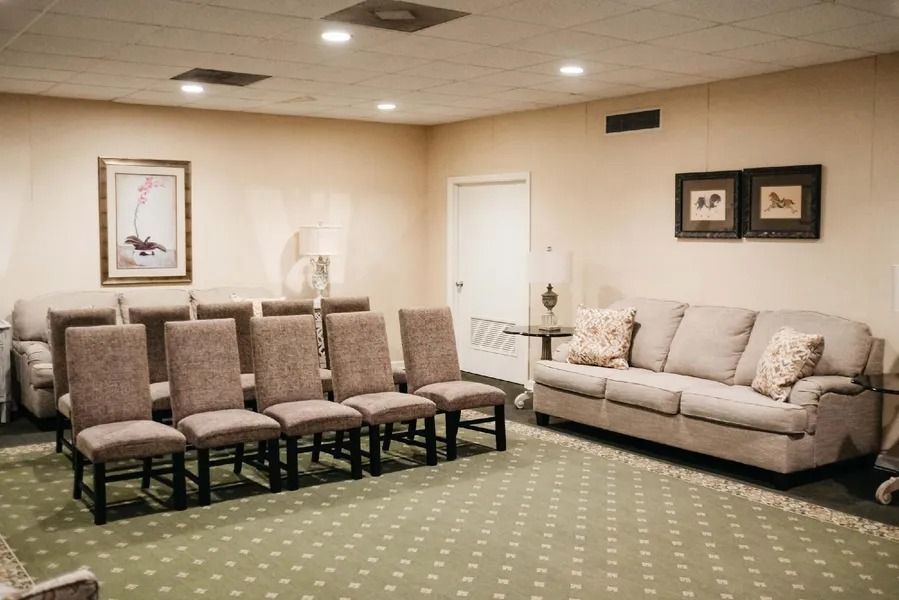 Funeral home visitation room with chairs, sofa, and artwork. Green carpet, beige walls.