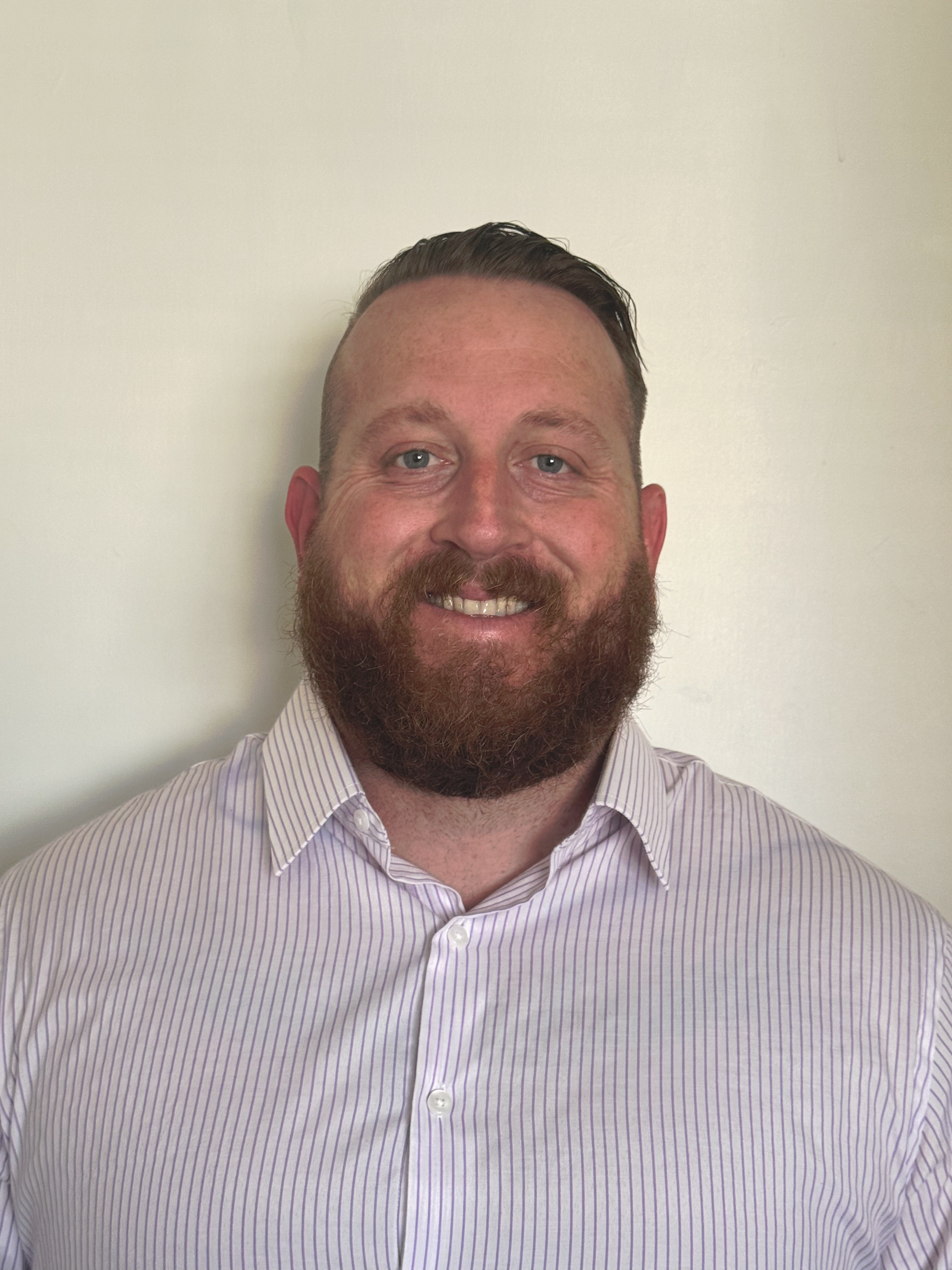 A man with a beard is wearing a striped shirt and smiling.