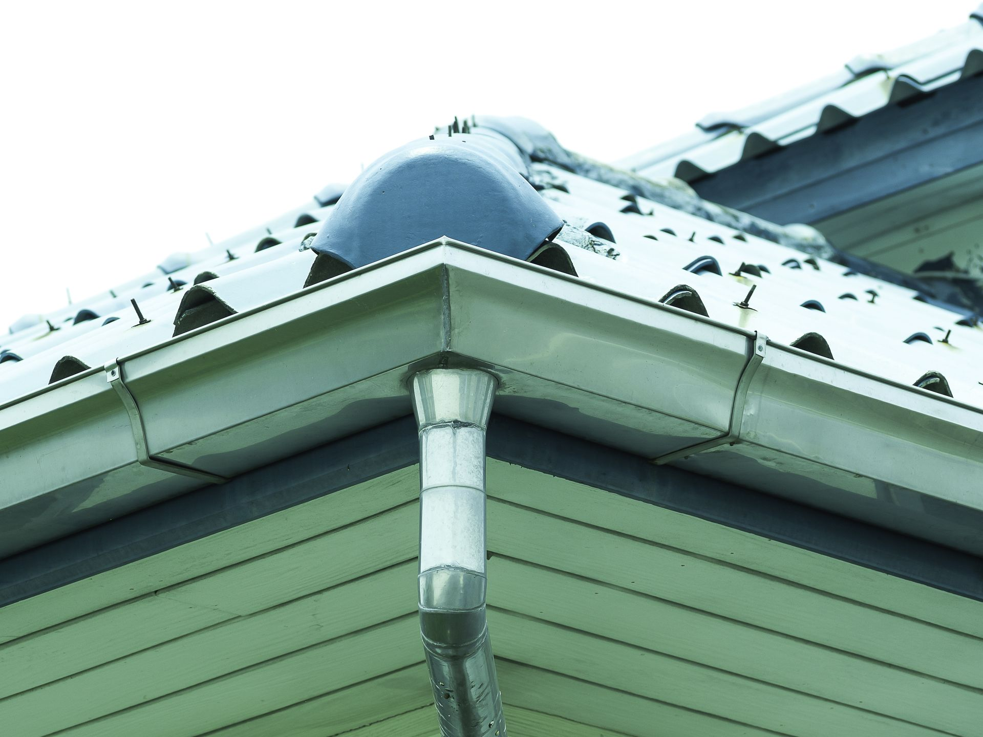Close-up of a house roof edge with a white gutter downspout and snow-covered shingles Close-up of a house roof edge with a white gutter downspout and snow-covered shingles