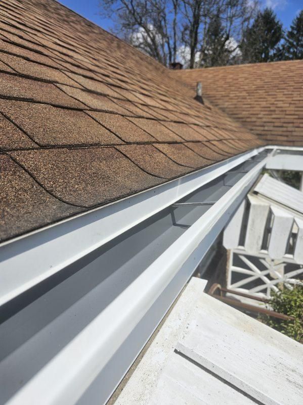 A man is standing on a ladder fixing a gutter on a house.