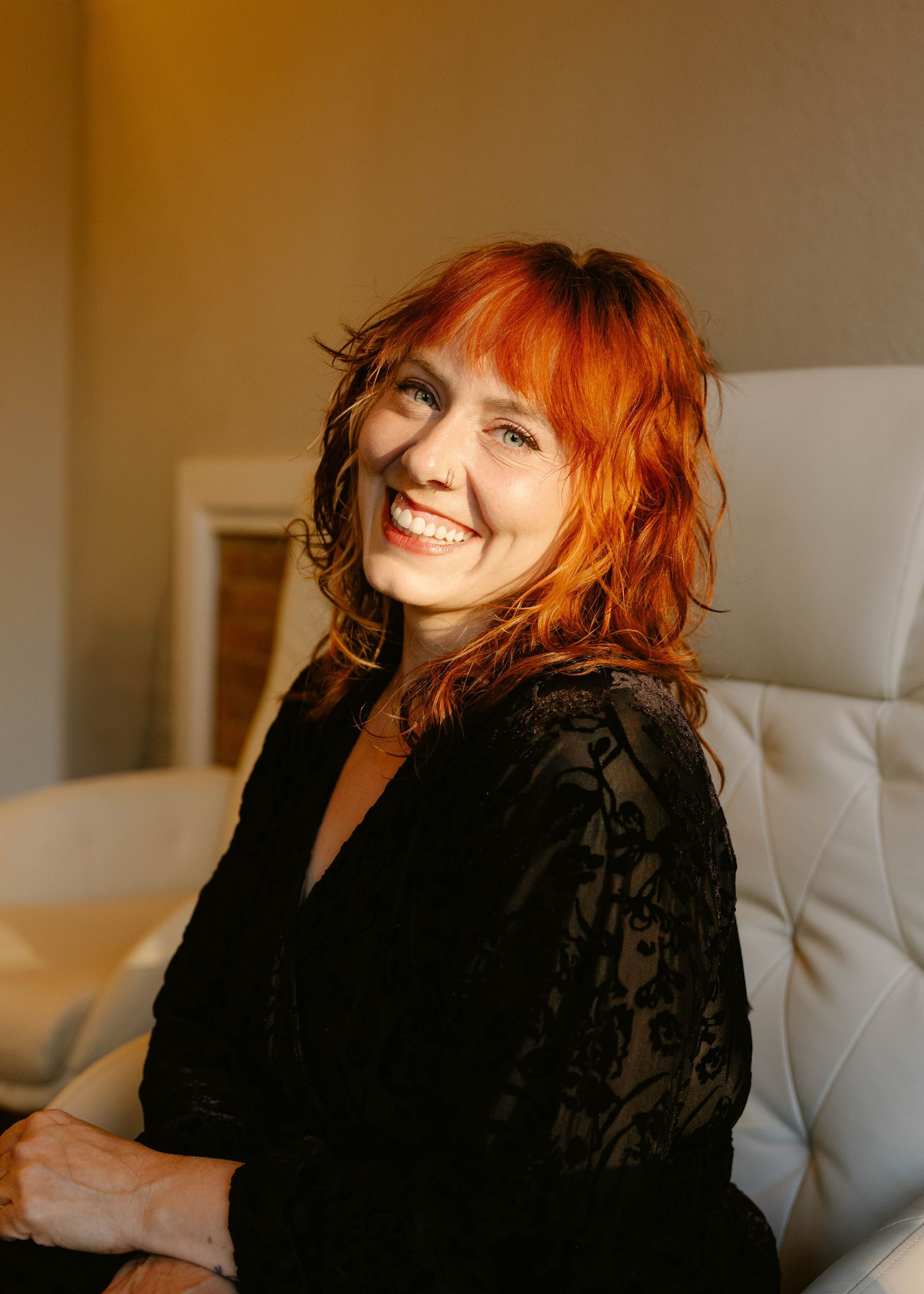 Kayla Robbins — Laramie, Wy — Luna Salon & Spa Smiling woman in a black top standing indoors against a light wall