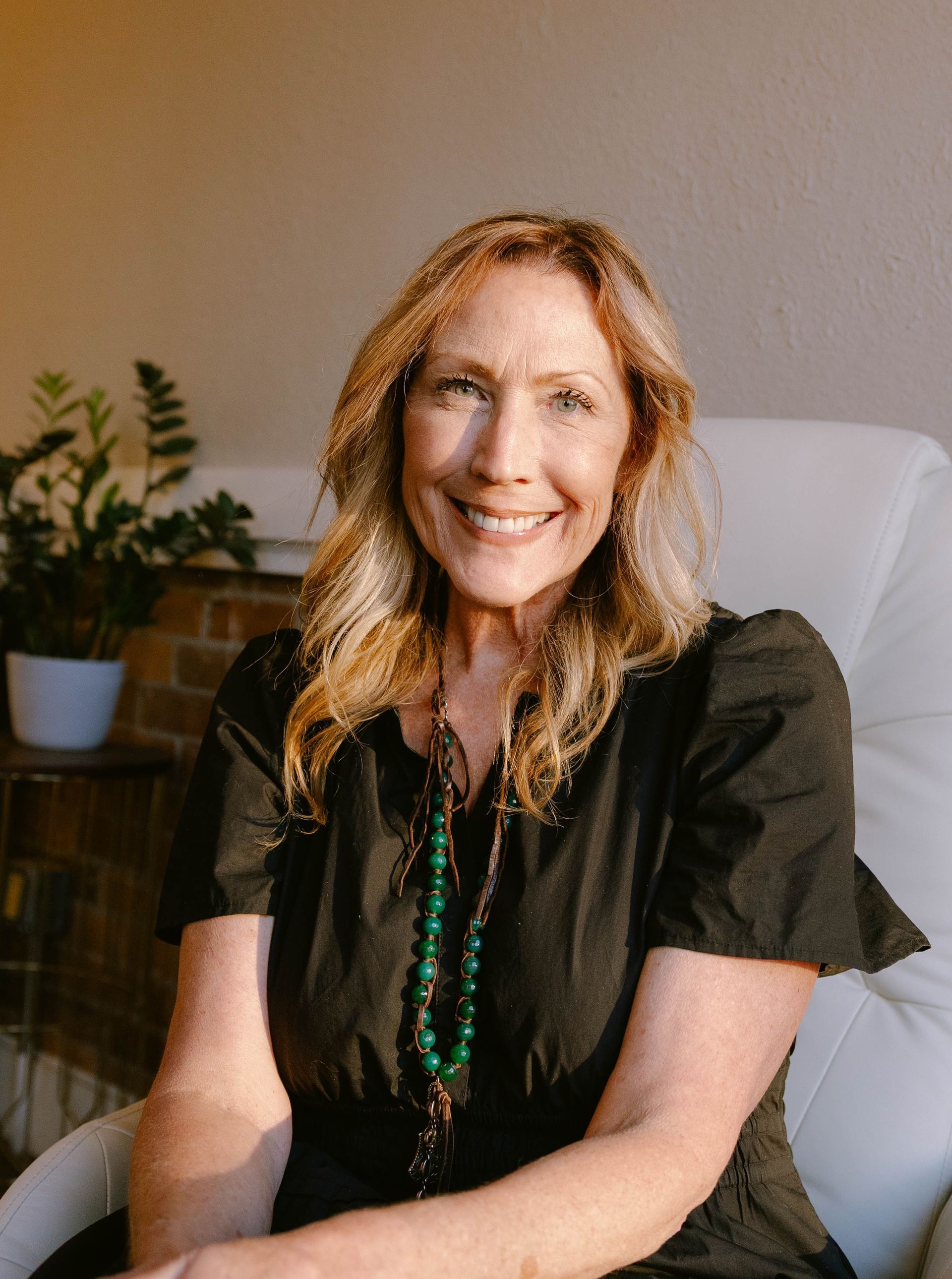 Heidi Little — Laramie, Wy — Luna Salon & Spa Smiling blonde woman in a black top, seated indoors against a light wall.
