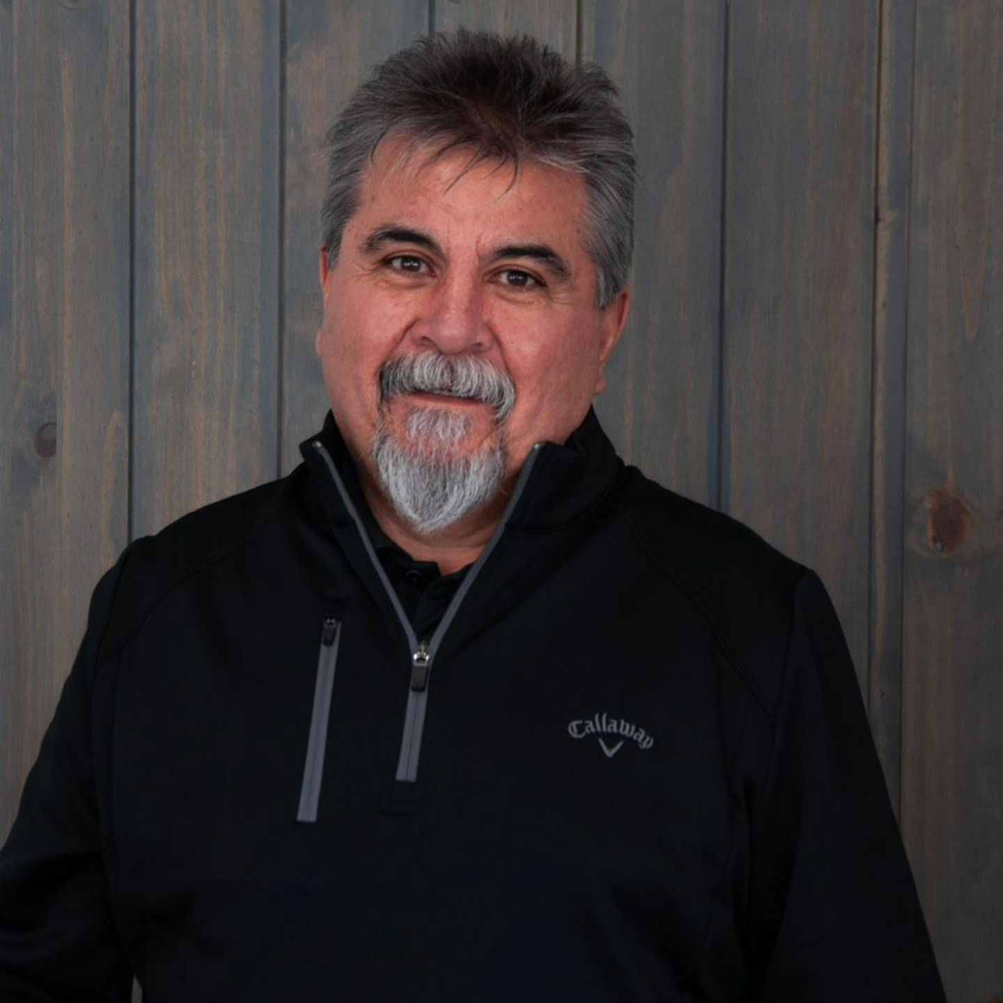 Picture of a Girl with a Black Shirt and Blonde Hair — Laramie, Wy — Luna Salon & Med Spa Man in a black zip-up jacket standing against a gray wood-paneled wall, smiling at the camera