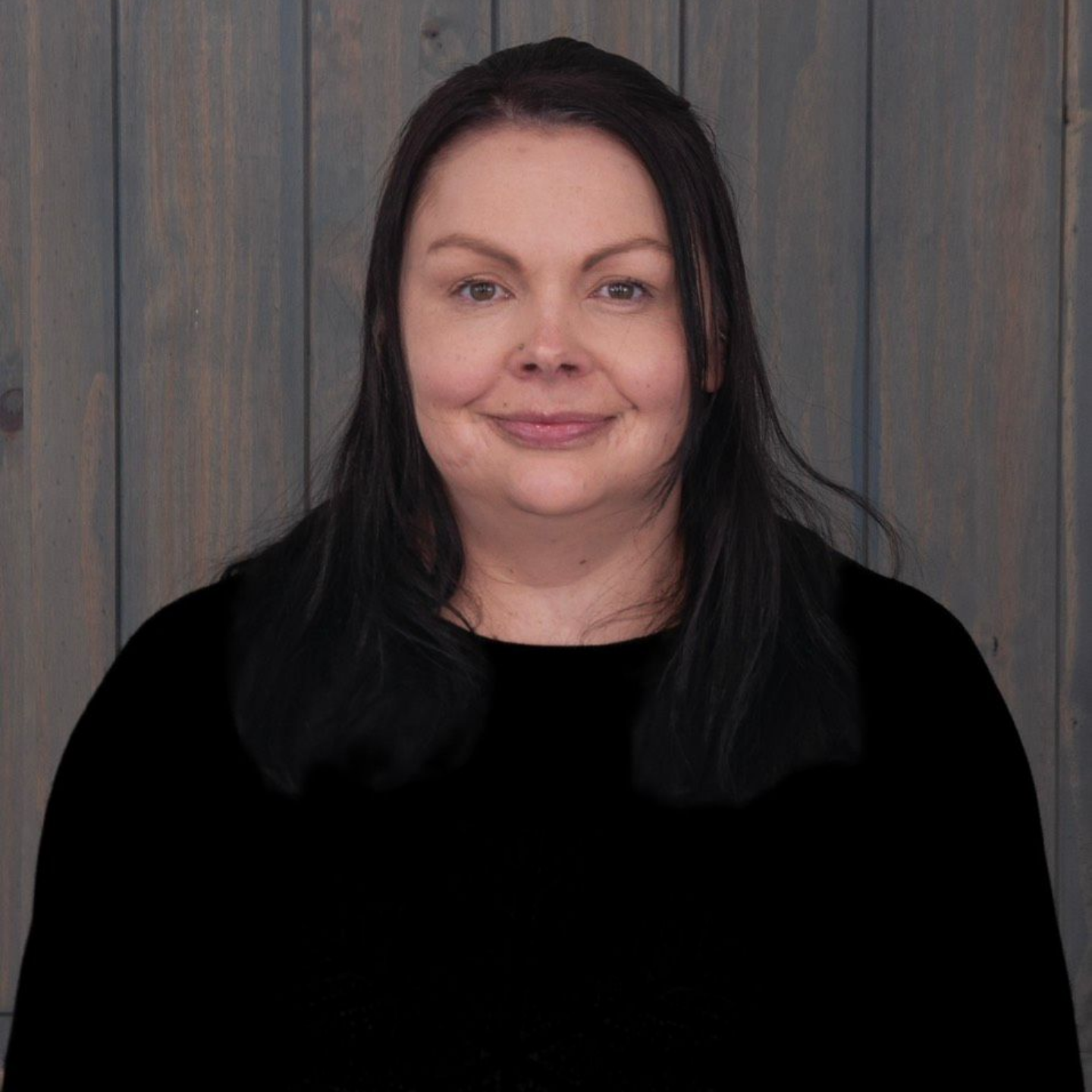 Picture of a Girl with a Black Shirt and Blonde Hair — Laramie, Wy — Luna Salon & Med Spa Portrait of a woman with dark hair, wearing a black top, standing against a gray wooden background