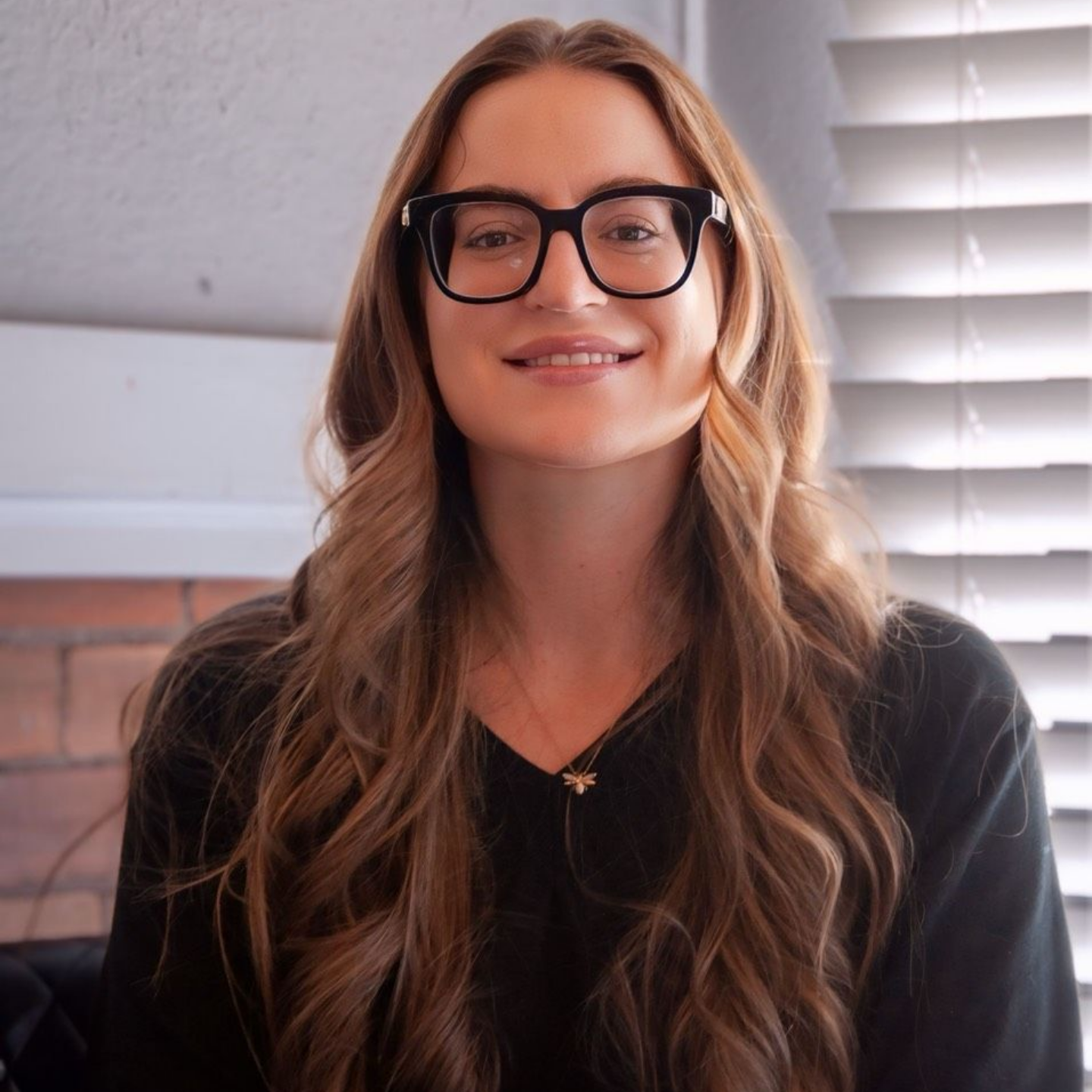 Megan Dreyer — Laramie, Wy — Luna Salon & Spa Woman with long wavy hair and glasses smiling indoors near a window
