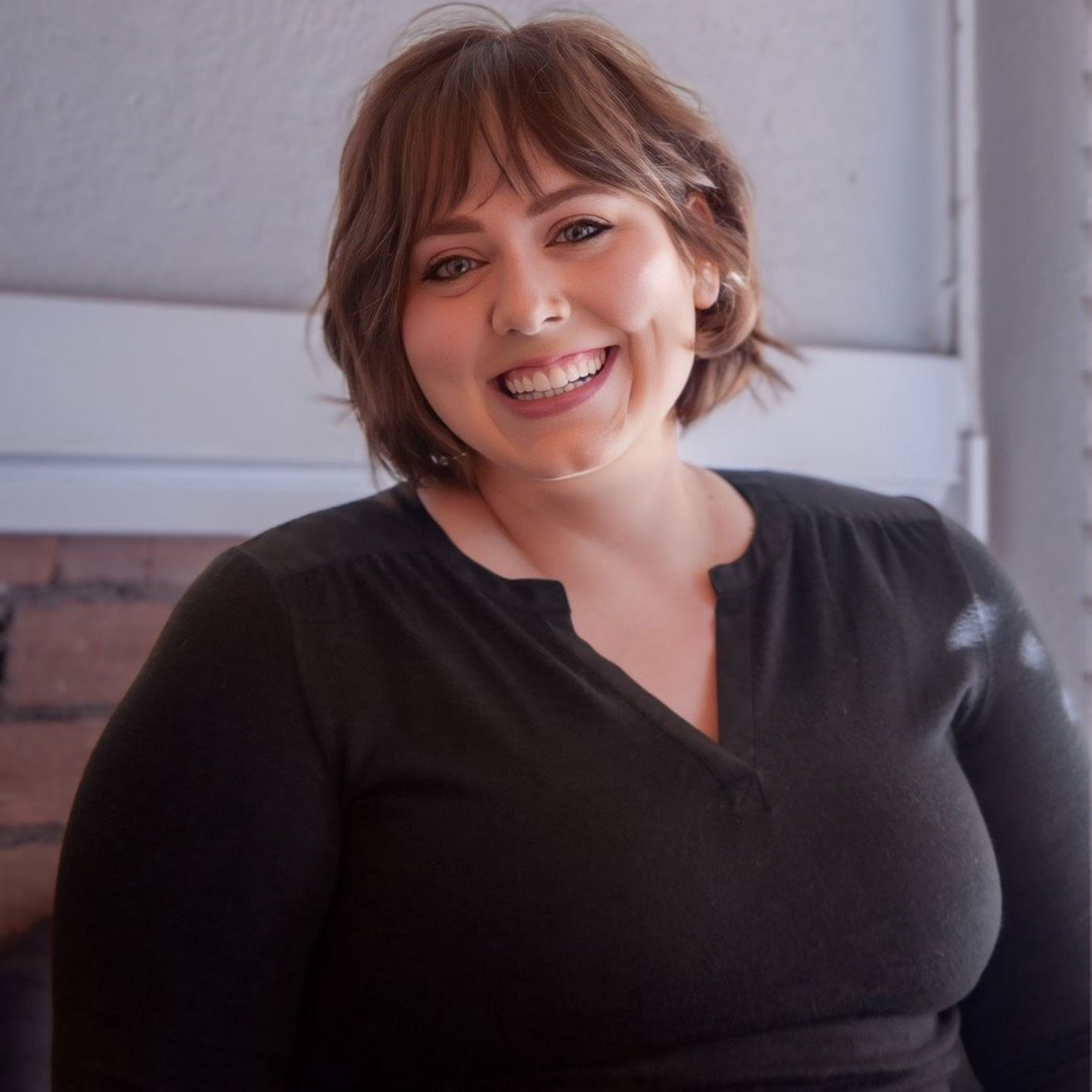 Kayla Robbins — Laramie, Wy — Luna Salon & Spa Smiling woman in a black top standing indoors against a light wall