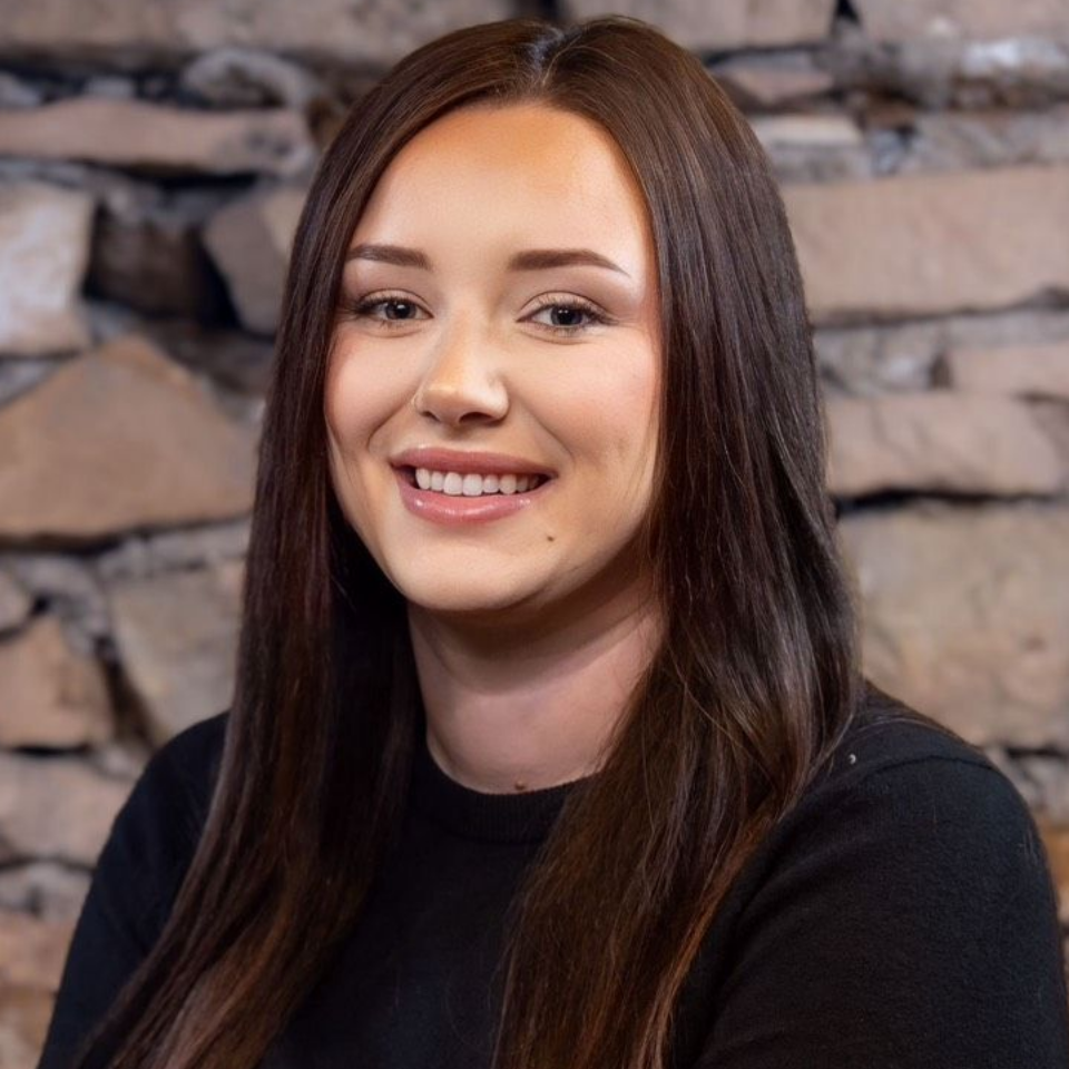 Portrait of a smiling woman with long dark hair in front of a stone wall