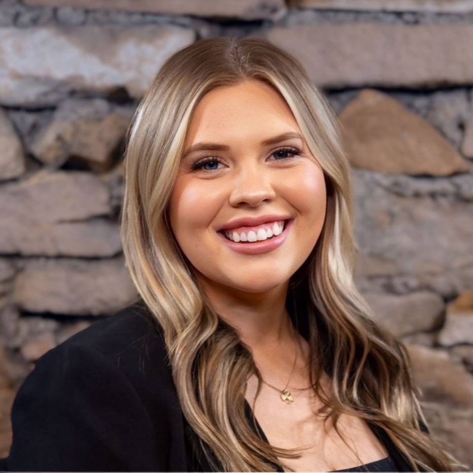 Smiling blonde woman in a black top posing in front of a stone wall