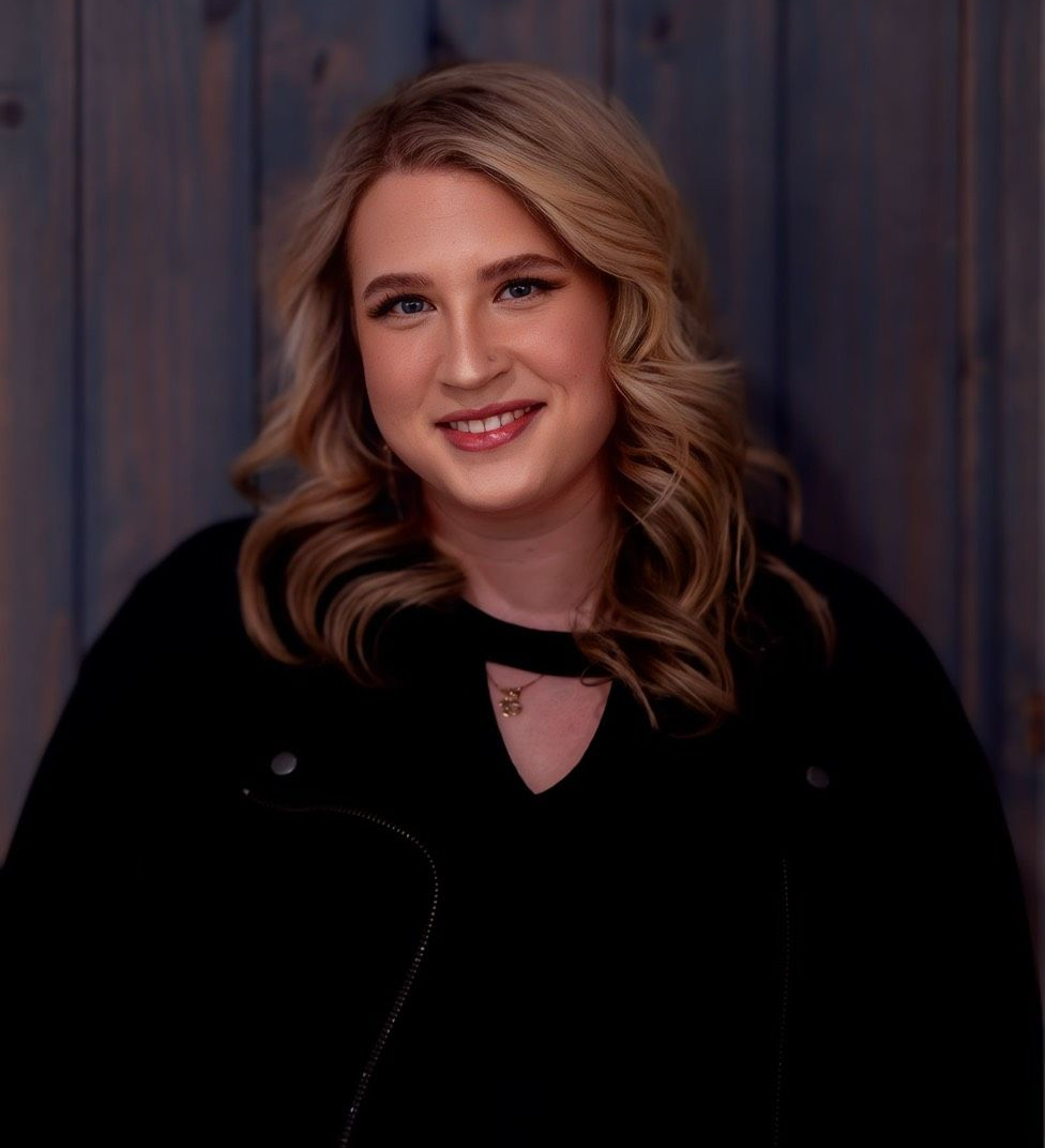 Smiling woman in a black top against a dark wooden backdrop