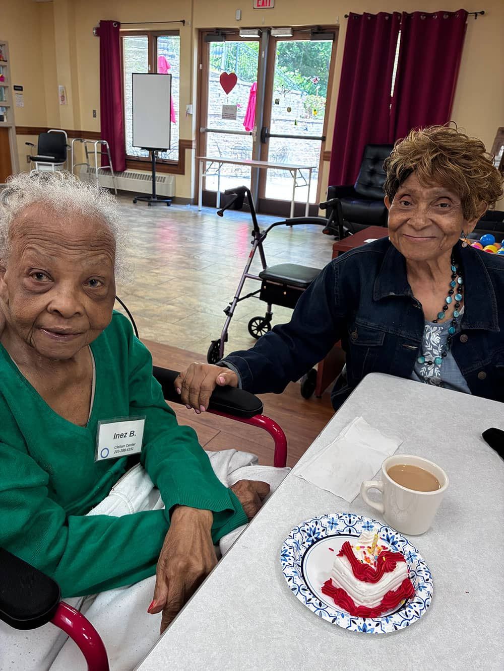 Two seniors seated at a table with dessert and coffee in a bright community room