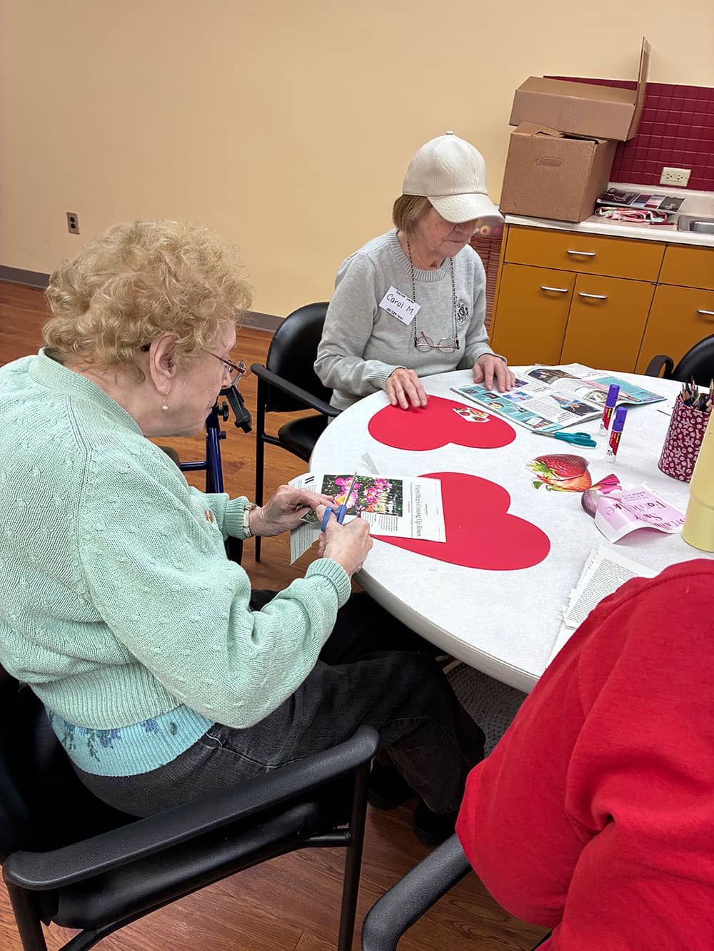 People sitting at a table crafting red-and-white paper shapes in a classroom or activity room