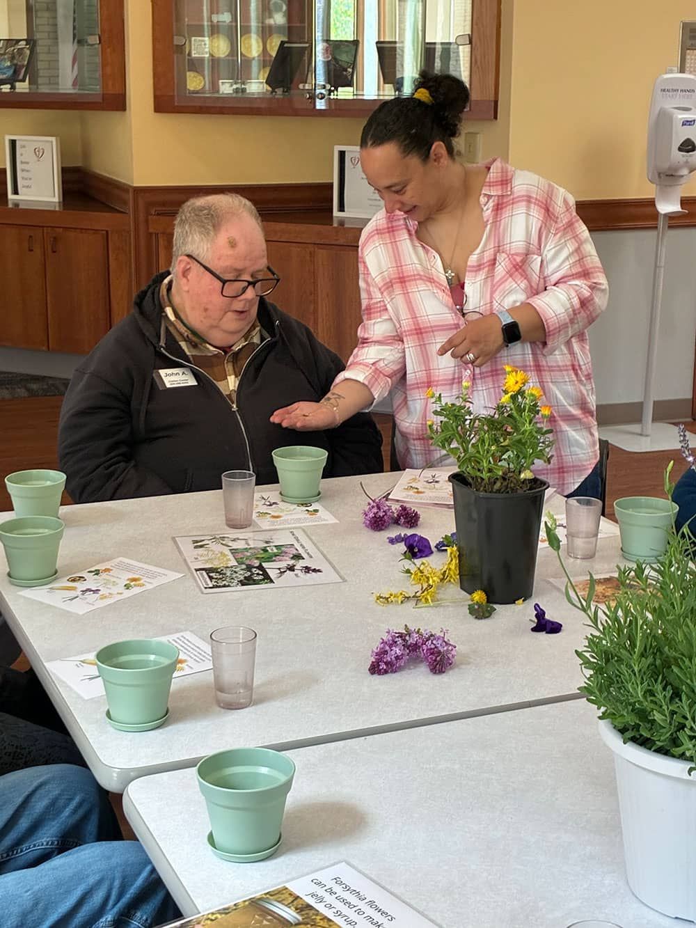 Two people at a table arranging flowers in a bright indoor room