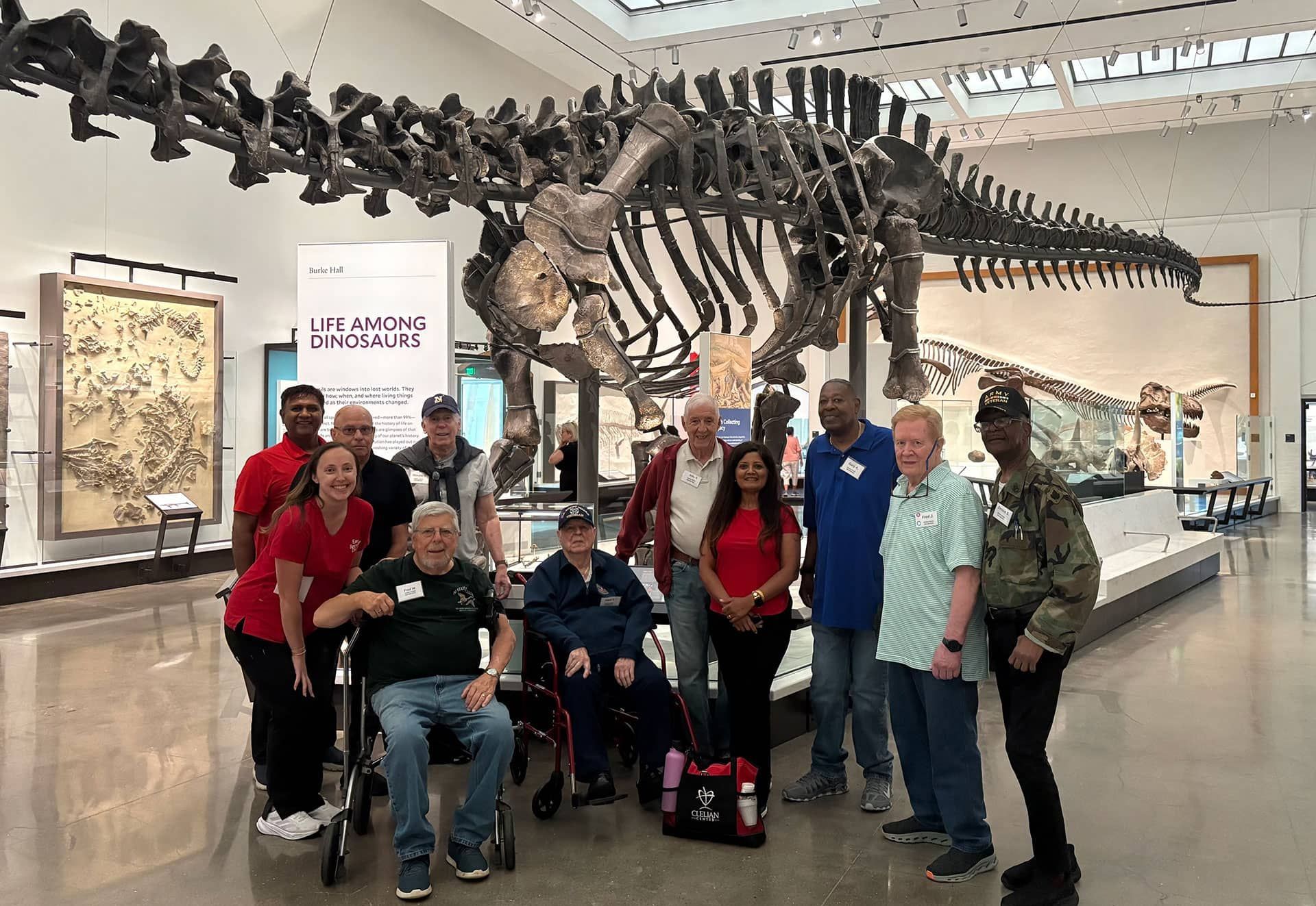 Group posing in a museum beside a large dinosaur skeleton exhibit