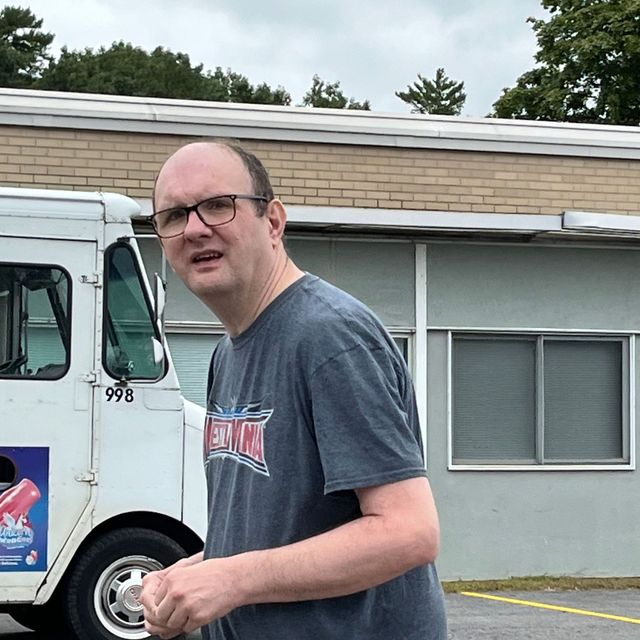 A man wearing glasses is standing in front of a food truck