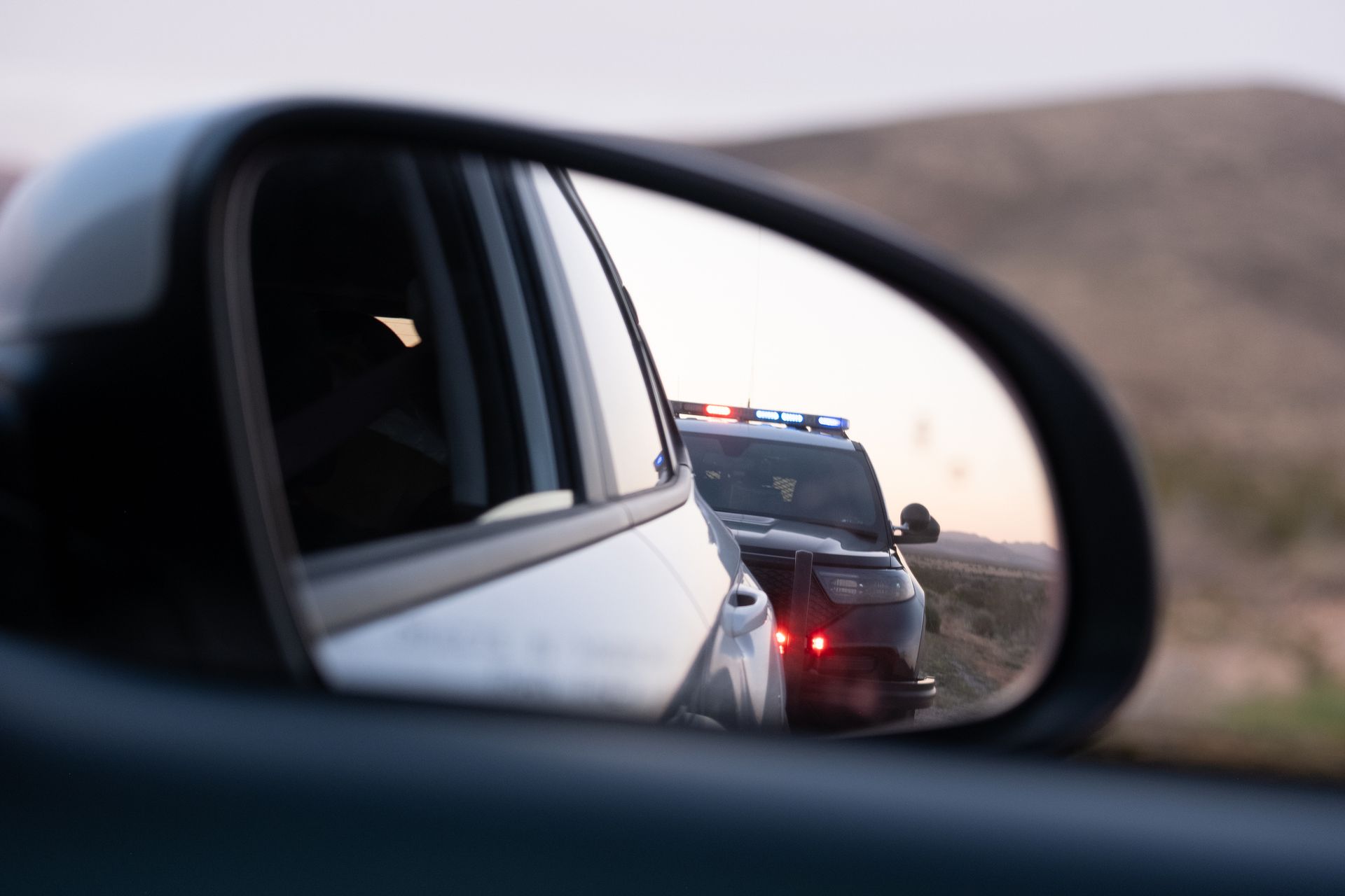 a police car stopped behind a car, as seen through a side-view mirror
