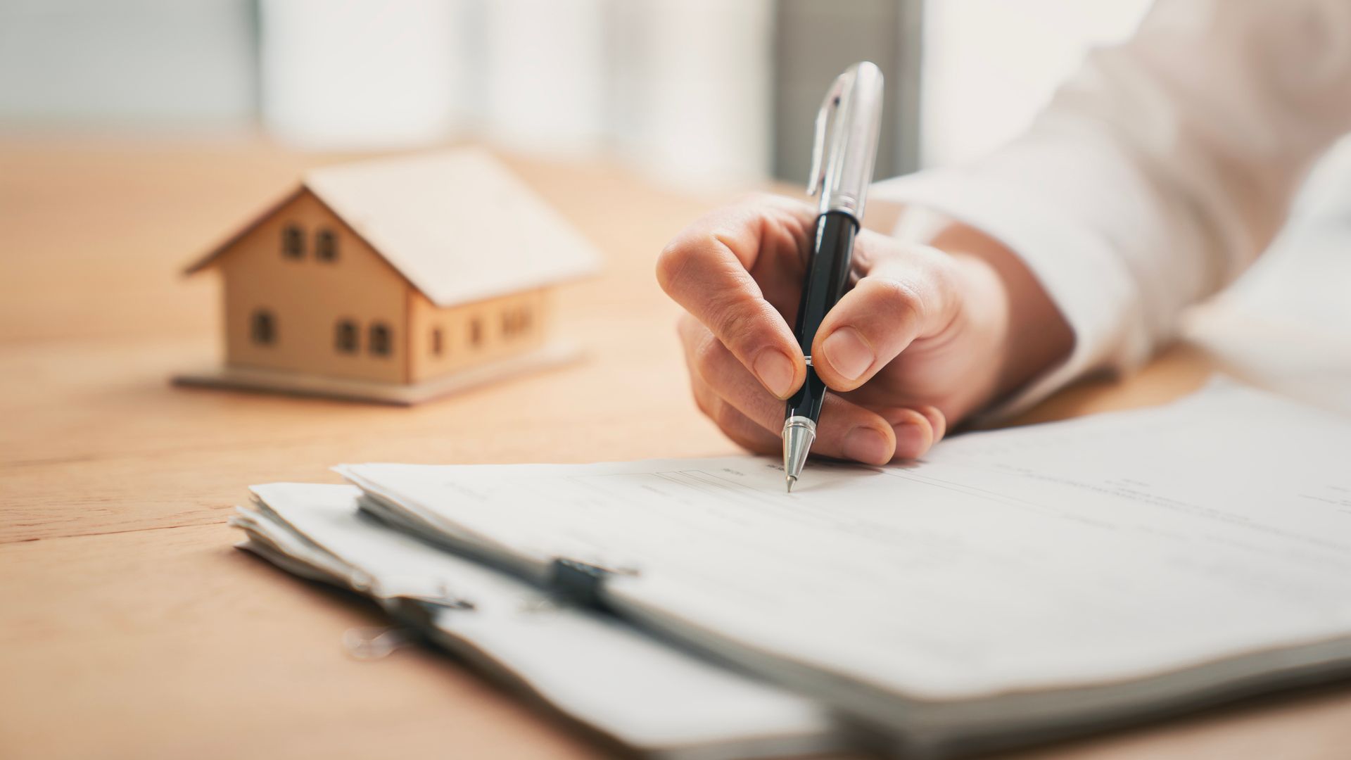 a person signing documents, with a small house figurine in the background