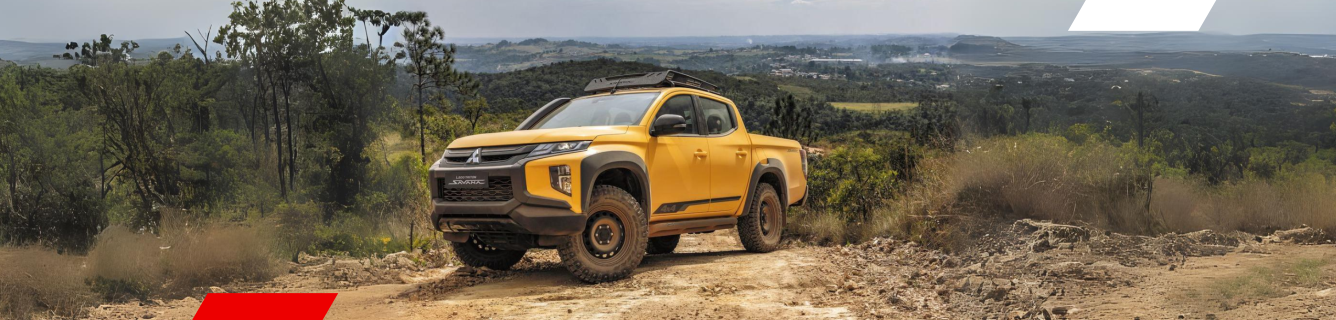 Caminhão amarelo trafegando em uma estrada de terra em uma paisagem montanhosa.