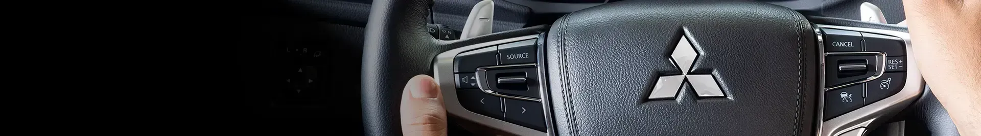 Volante de um carro com o logotipo da Mitsubishi, mão no volante.