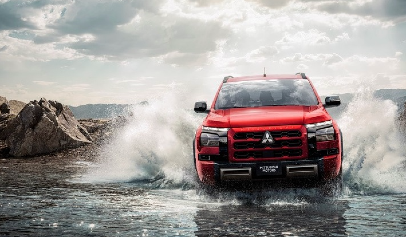 Uma caminhonete Mitsubishi vermelha atravessando um rio, espirrando água.