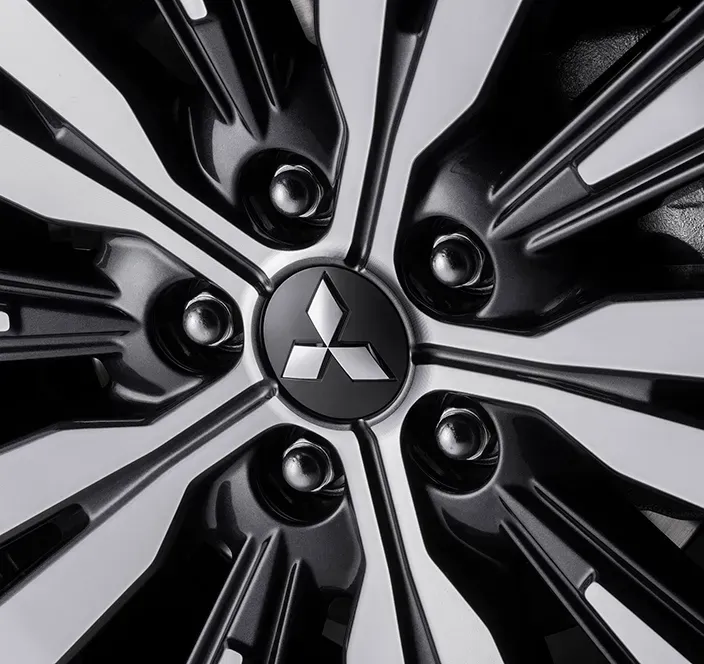 Detalhe de uma roda de carro com o logotipo da Mitsubishi no centro; raios e parafusos pretos e prateados são visíveis.