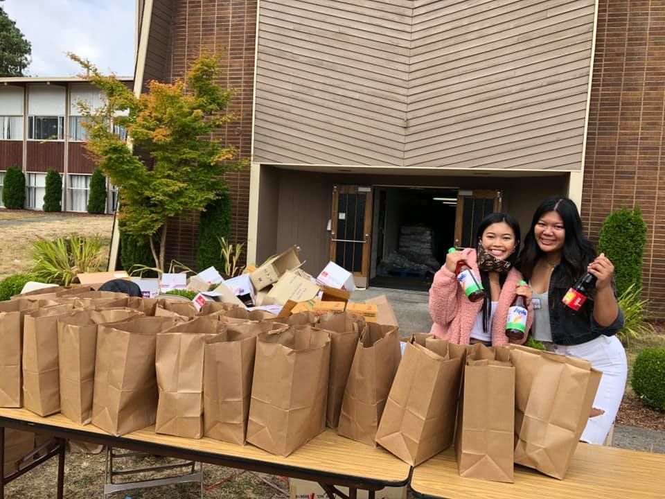 Two women are standing in front of a table filled with paper bags.