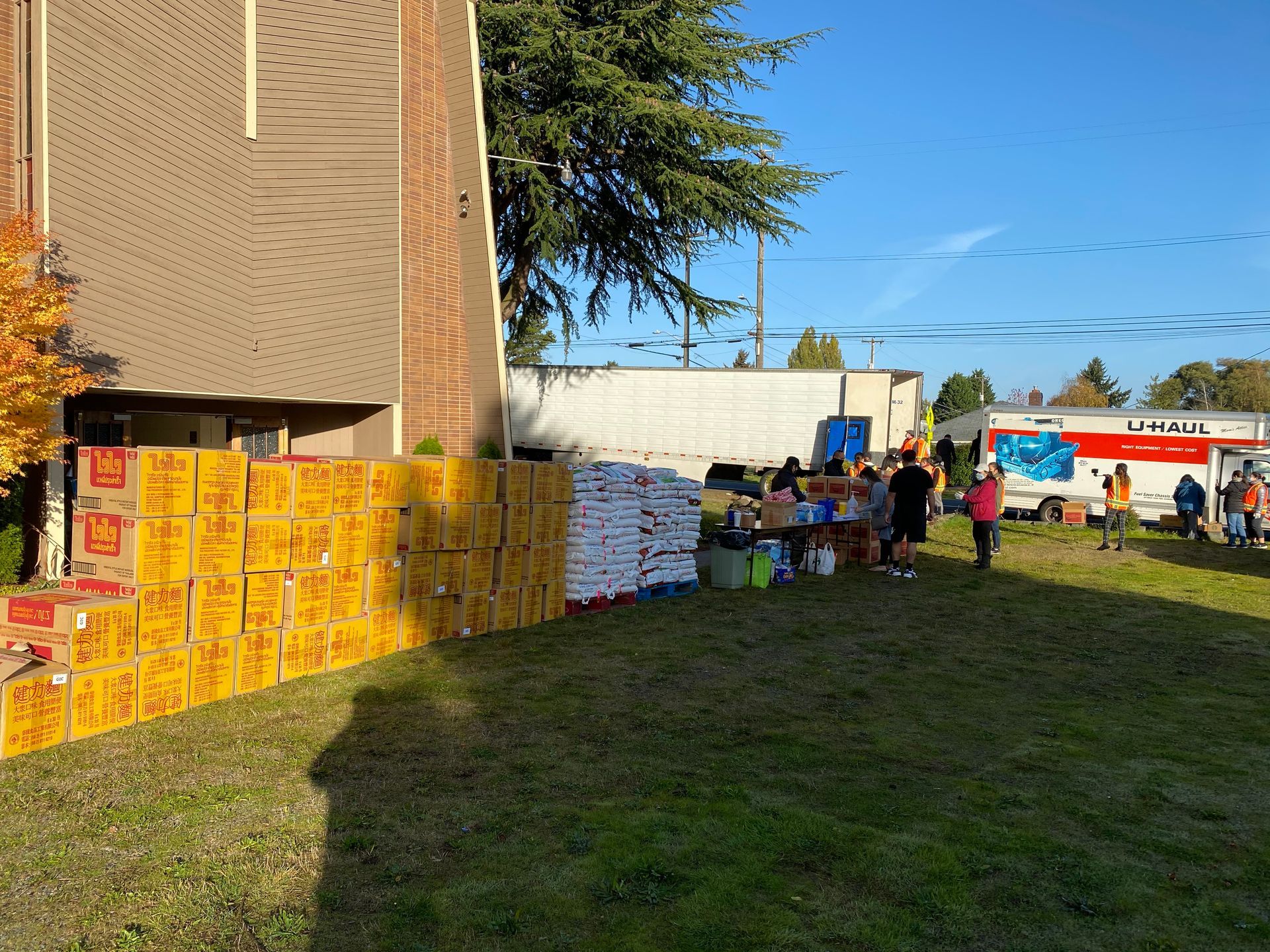 A bunch of boxes are stacked on top of each other in a grassy area in front of a building.