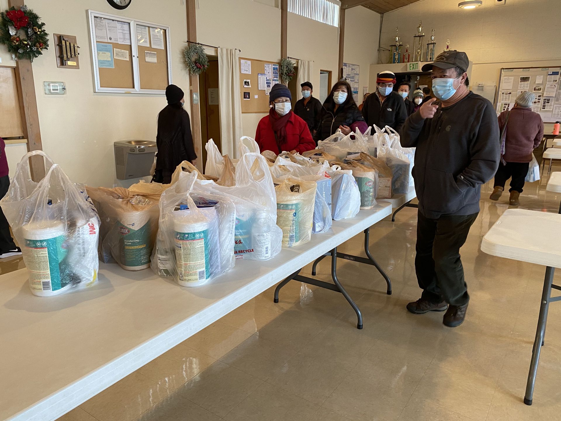 A group of people wearing masks are standing around a table filled with bags of food.