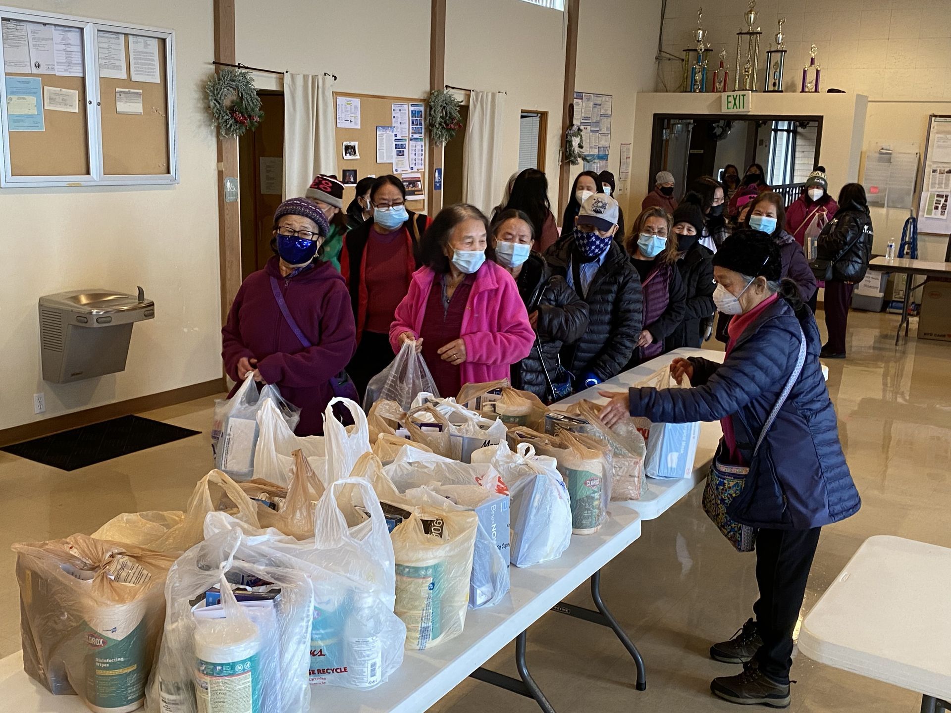 A group of people wearing face masks are standing around a table filled with bags of food.