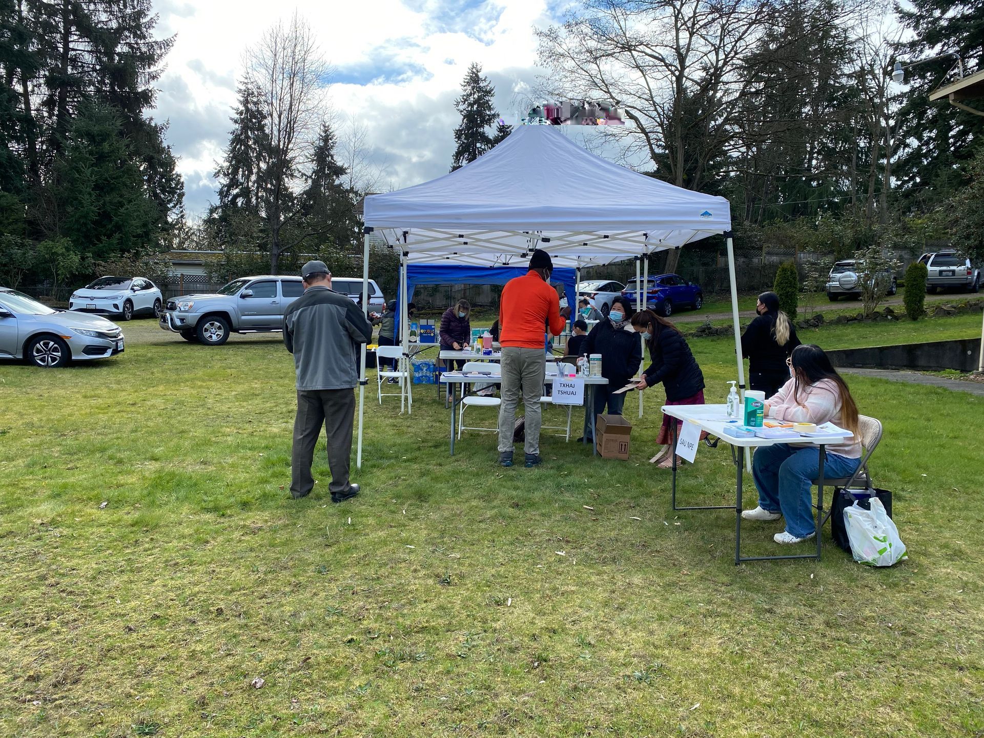 A group of people are standing under a tent in a grassy field.